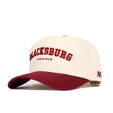 The Blacksburg Hometown Hat by No Rivals is a cream snapback with a maroon bill, made from premium cotton. It features "BLACKSBURG" in maroon and gold embroidery, with "VIRGINIA" stitched below in smaller maroon lettering.