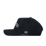 The UNT Night Mode Hat by No Rivals is a black snapback hat shown from the side, featuring white embroidered logos with “NR” near the back and partially visible white text on the front.