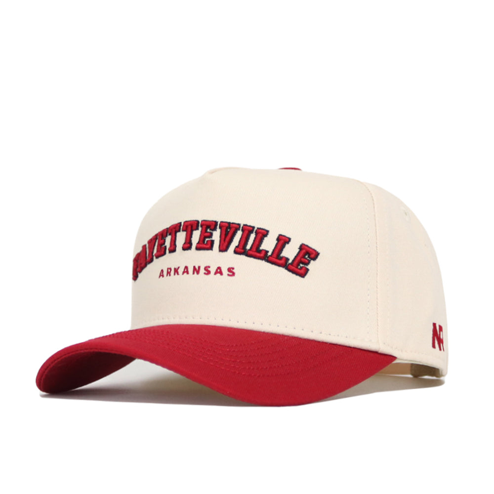 The No Rivals Fayetteville Hometown Hat is a cream cotton cap with a red brim, featuring "FAYETTEVILLE" in red and black above "ARKANSAS" in smaller red print. This structured fit offers comfort and classic style.
