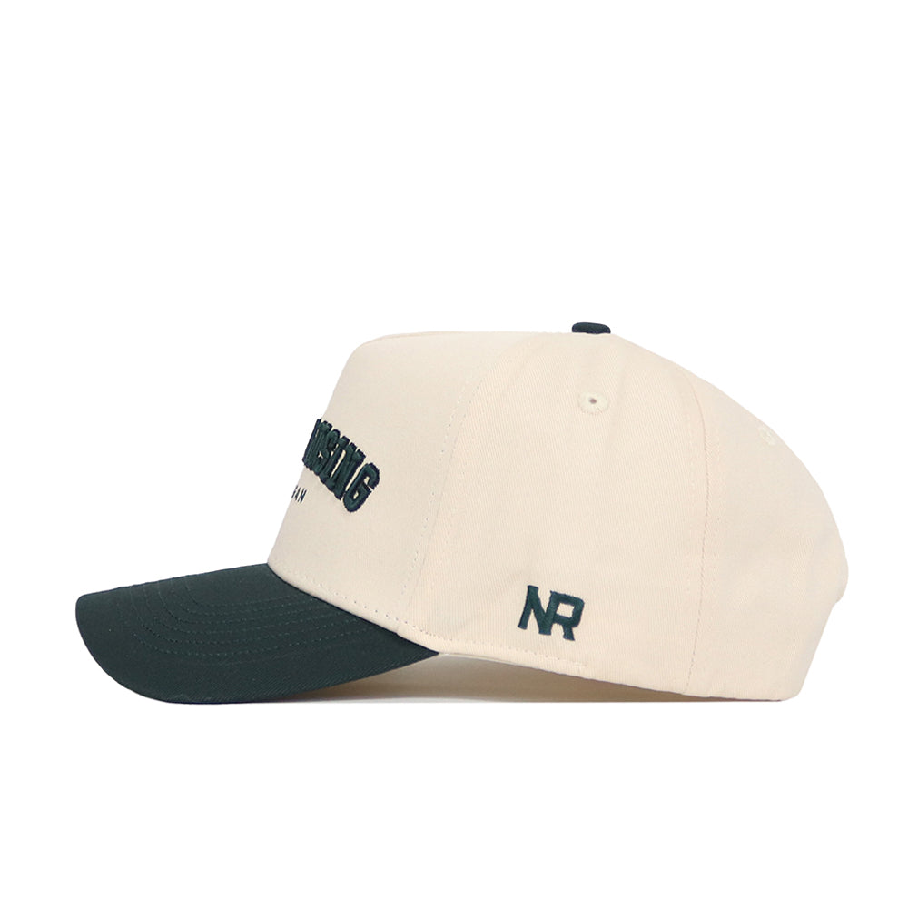 The No Rivals East Lansing Hometown Hat is a structured beige cotton cap with a dark green curved brim, dark green embroidered front text, NR initials on the side, and an adjustable snapback for comfort and style.
