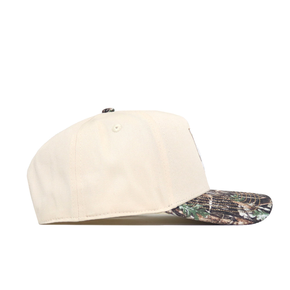 The Oregon Camo Connector Hat by No Rivals is a beige snapback with a curved brim, green and brown camo pattern, perfect for gameday style. Shown from the side against a white background.