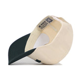 The East Lansing Hometown Hat by No Rivals is beige with a dark green brim, shown upside down to reveal its structured interior, NO RIVALS tag, QR code, and classic snapback design.