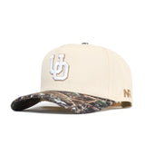 The Oregon Camo Connector Hat by No Rivals features a beige snapback design, white UD letters on the front, a brown camo brim, and gold NF embroidery—ideal for gameday with standout embroidered logos.