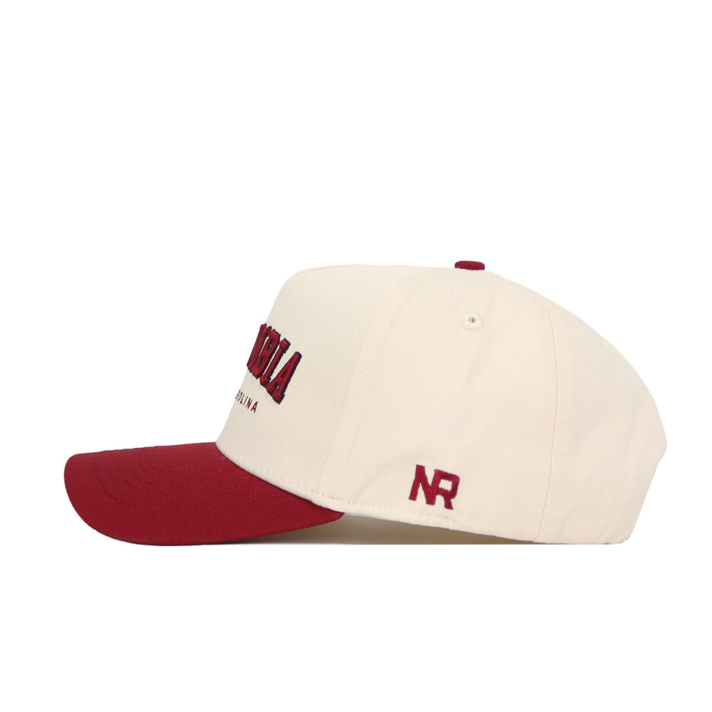 The No Rivals Columbia Hometown Hat is a cream snapback with a maroon brim, crafted from high-quality cotton. It features maroon NR initials embroidered on the side and maroon with black embroidery on the front for a structured fit.