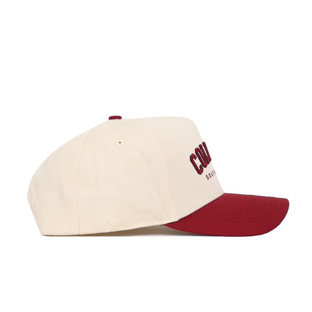 The Columbia Hometown Hat by No Rivals is a beige cotton baseball cap with a structured fit, maroon brim and button, and maroon embroidered front text, displayed in side profile against a white background.