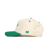 The Oregon Vintage Hat by No Rivals is a cream-colored cotton baseball cap with a green brim, green stitching, and "NR" embroidered in green near the back. Shown in profile against a white background.