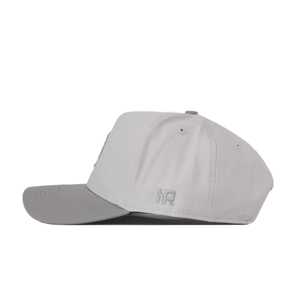 The No Rivals Boise State Graphite Hat is a light gray baseball cap with a slightly darker gray brim, shown from the side. It features small ventilation holes, a subtle embroidered logo near the back, and a classic snap back closure—perfect for finishing off your gameday look.
