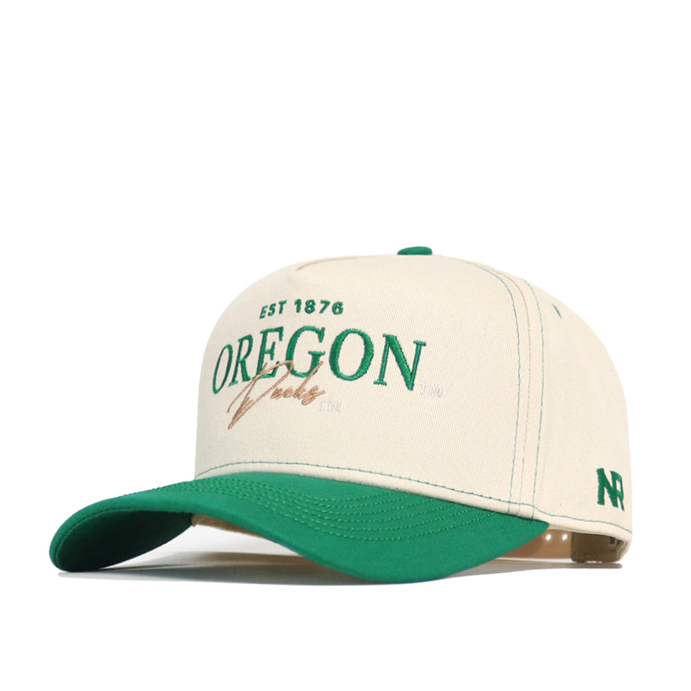 The Oregon Vintage Hat by No Rivals is a cream and green baseball cap with an embroidered OREGON Ducks EST 1876 logo, NP stitched on the side, and a green curved brim. This officially licensed snapback is ideal for fans.