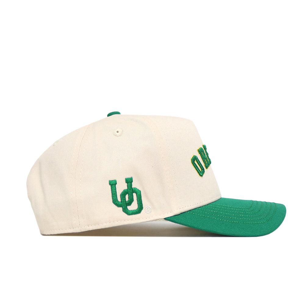 The No Rivals Right Side Up Oregon Hat - Classic is a cream snapback with a green brim, green embroidered UD initials on the side, and partially visible green lettering on the front.