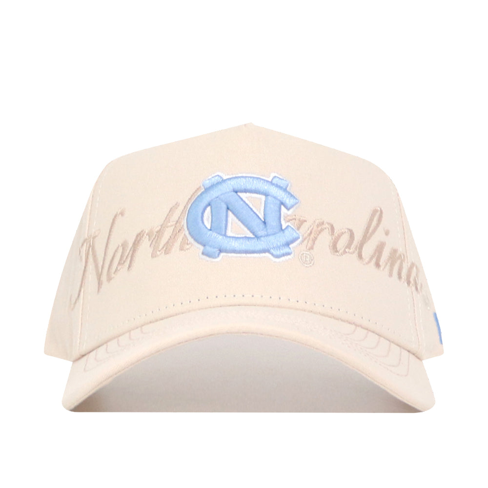 The No Rivals North Carolina Stacked Hat is a beige cotton baseball cap featuring "North Carolina" in script and a bold blue UNC logo above the brim. It has an adjustable snapback and is officially licensed.