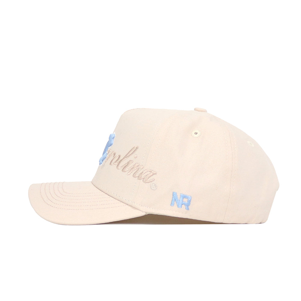 The North Carolina Stacked Hat by No Rivals is a beige cotton cap with blue embroidered text and NR on the side. It features a curved brim, ventilation eyelets, and an adjustable snap back for the ideal fit.