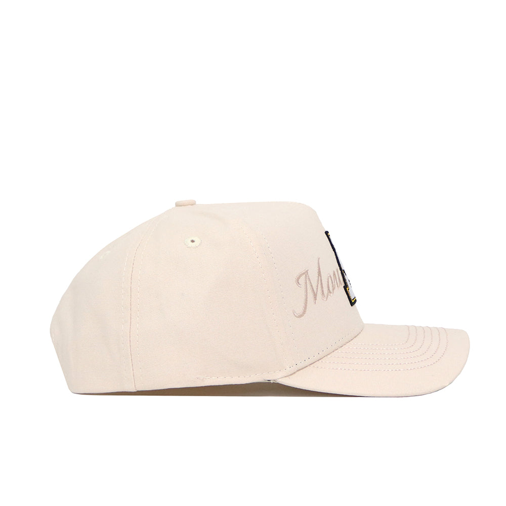 The No Rivals App State Stacked Hat is a beige snapback baseball cap with subtle embroidered text and a small black-and-gold patch on the front. Made from high-quality cotton, it offers a comfortable, structured fit.