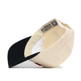 The Athens Hometown Hat by No Rivals is a cream snapback with a black bill, shown from below to reveal its cotton build, structured fit, and inner band featuring “NO RIVALS” and a QR code. The cap rests on its side highlighting interior details.