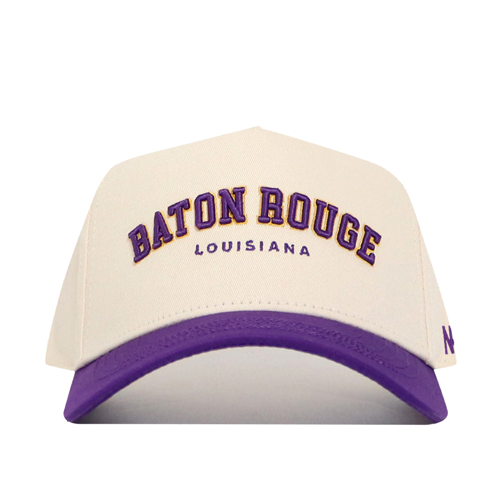 The No Rivals Baton Rouge Hometown Hat is a white cotton baseball cap with a purple brim, featuring BATON ROUGE in purple and gold and LOUISIANA in small purple letters on the front. It has a structured fit and snapback closure for style and comfort.