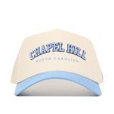 The No Rivals Chapel Hill Hometown Hat is a beige cotton cap with a light blue brim, featuring "CHAPEL HILL" in large blue letters and "NORTH CAROLINA" below.