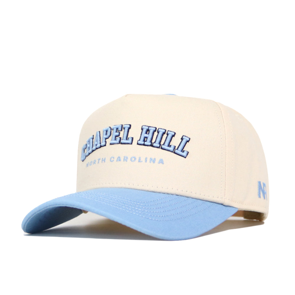 The No Rivals Chapel Hill Hometown Hat is a beige snapback with a light blue bill, featuring "Chapel Hill" and "North Carolina" in blue letters on the front. Made from durable, comfortable cotton fabric.