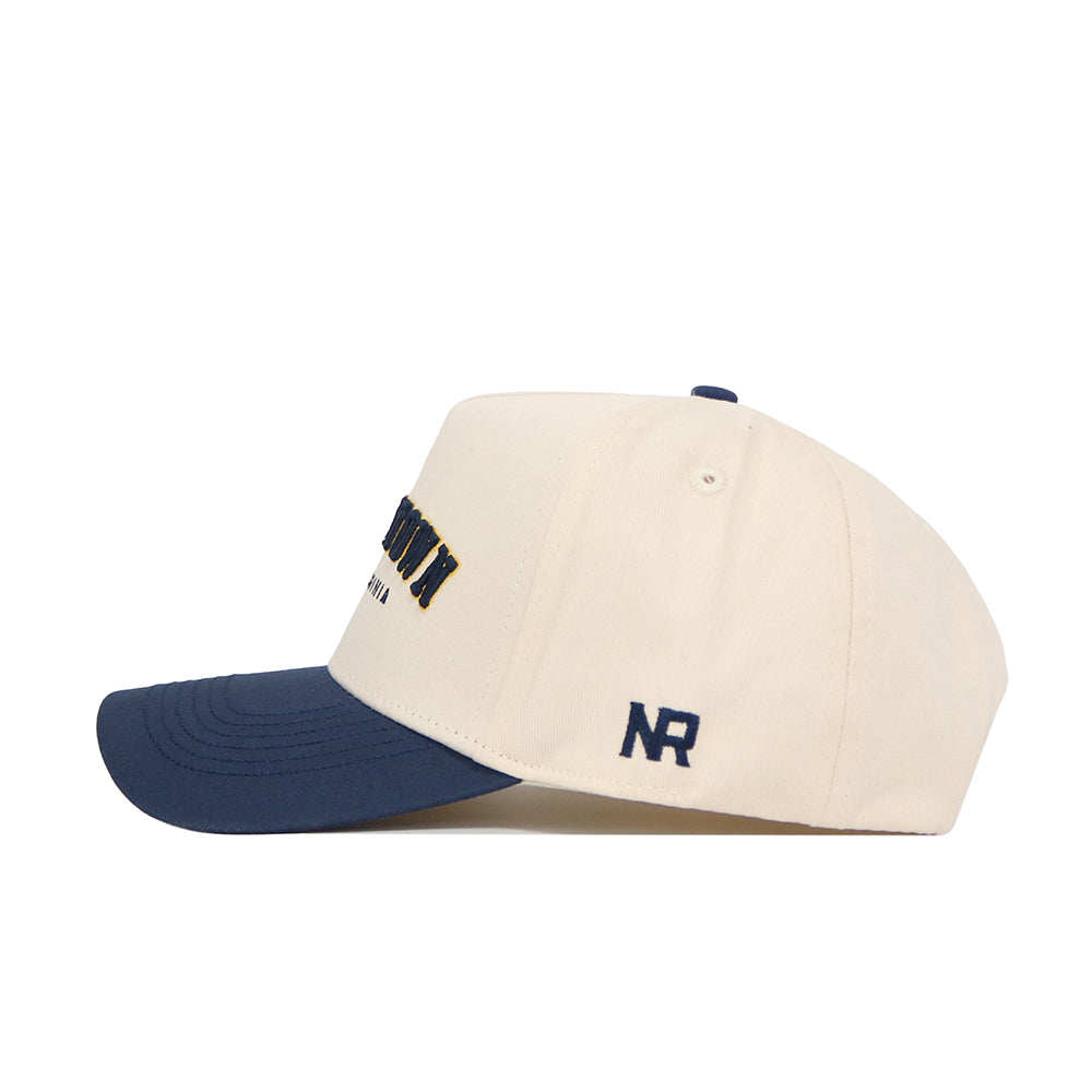 The No Rivals Morgan Town Hometown Hat is a structured cream cap with a navy brim, front embroidery, NR initials on the side, high-quality cotton construction, and a classic snapback closure.