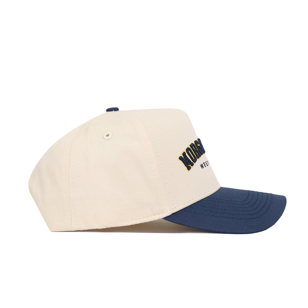 The No Rivals Morgan Town Hometown Hat is a cream snapback with a navy brim and yellow/navy embroidered front text. Made from premium cotton, it features a structured fit and is displayed side-view against a white background.