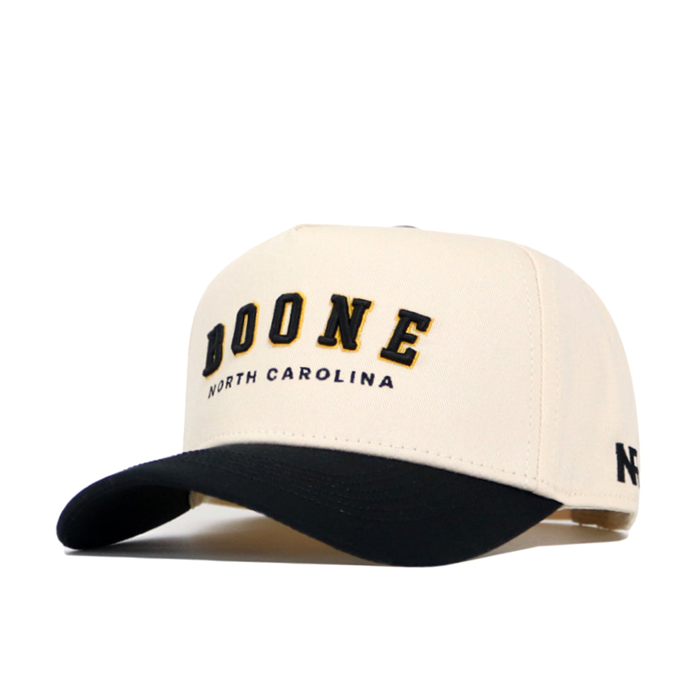 The Boone Hometown Hat by No Rivals is a cream and black snapback with "BOONE NORTH CAROLINA" embroidered in black and gold, a curved black brim, structured cotton fit, and an NC logo on the side.