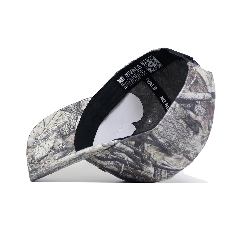 The Montana State Outland Hat by No Rivals is shown upside down, displaying its camouflage pattern, a black inner band with the NO RIVALS logo, and a white paper insert inside the crown.