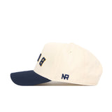 The Upside Down BUCS Hat - ETSU - Classic Colors by No Rivals features a cream snapback design with a navy brim, NR embroidered in navy on the side, and partially visible dark lettering on the front.