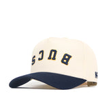 The Upside Down BUCS Hat - ETSU by No Rivals is a cream snapback with a navy brim and BUCS embroidered in gold and navy on the front, crafted from high-quality cotton for comfort and style.