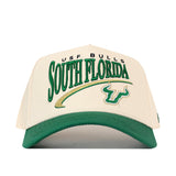 Cream-colored No Rivals USF Stride Hat with a green brim, featuring embroidered SOUTH FLORIDA text, the USF BULLS logo, and a bull horn icon in green and gold.