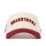 This officially licensed No Rivals snapback is the Upside Down Charleston Hat - Classic, featuring a cream color with a red brim and “CHARLESTON” embroidered in arched red and gold letters across the front.