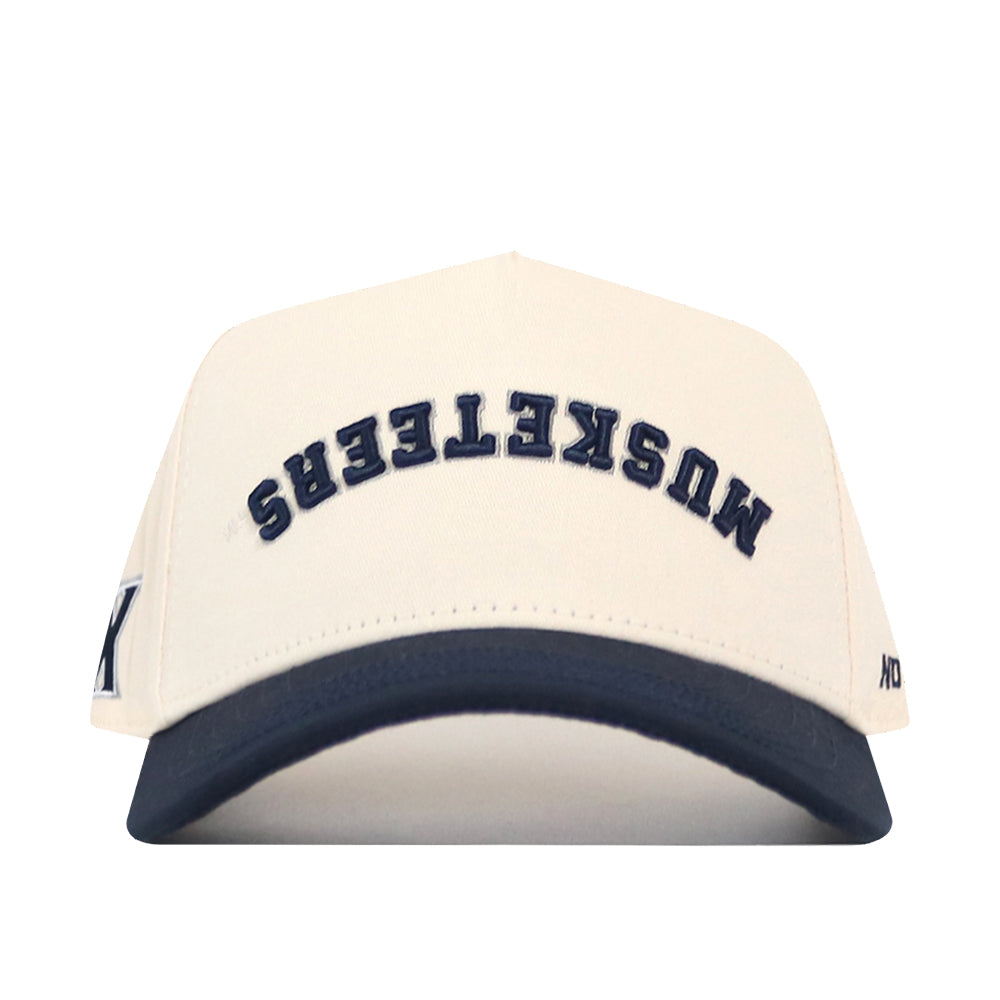 Add this No Rivals Xavier Musketeers | Upside Down Musketeers Hat - Classic to your collection—a cream-colored snapback baseball cap with a navy brim, featuring “MUSKETEERS” embroidered upside down in navy letters on the front for an officially licensed, standout look.