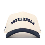Add this No Rivals Xavier Musketeers | Upside Down Musketeers Hat - Classic to your collection—a cream-colored snapback baseball cap with a navy brim, featuring “MUSKETEERS” embroidered upside down in navy letters on the front for an officially licensed, standout look.