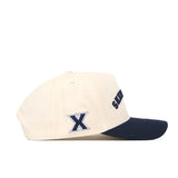 The No Rivals Xavier Musketeers | Upside Down Musketeers Hat - Classic is an officially licensed cream-colored baseball cap with a navy blue brim, showcasing a large embroidered X on the side and text on the front panel. Its classic snapback design offers adjustable comfort, perfect for any Xavier fan.