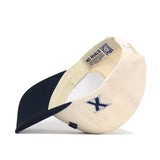 A beige and navy Xavier Musketeers | Upside Down Musketeers Hat - Classic by No Rivals is pictured inside out, revealing its interior tags and meticulous stitching, with an embroidered X logo prominently featured on the side. This snapback cap exemplifies No Rivals’ commitment to quality craftsmanship throughout.