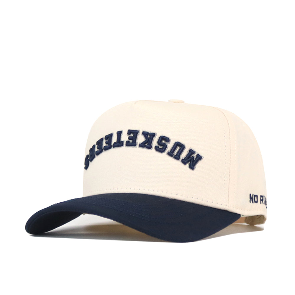 Introducing the Xavier Musketeers | Upside Down Musketeers Hat - Classic by No Rivals: this cream-colored snapback baseball cap features a navy brim, “MOSKETEERS” embroidered upside down in navy on the front, and “NO RIVALS” stitched discreetly on the side—an ideal addition to any Xavier Musketeers hat collection.