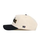 Side view of the App State Ballpark Hat by No Rivals, a cream cotton baseball cap with a black brim. Features embroidered text and designs on front and side, including NR initials above the ear. Structured fit.