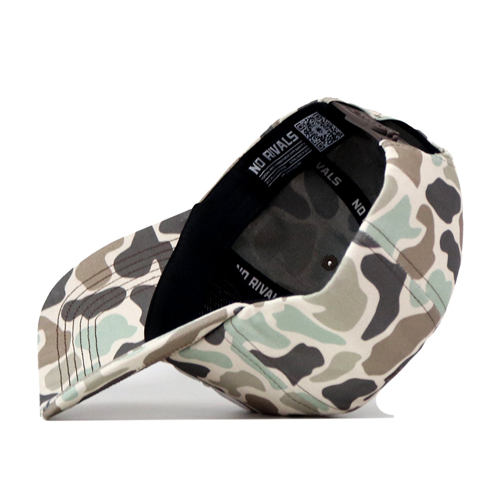 The Ole Miss Rebels Huntsman Hat by No Rivals, featuring a camouflage pattern and crafted from high quality cotton, is displayed on its side to reveal the inside label with “NO RIVALS” printed on it and a visible QR code under the brim.