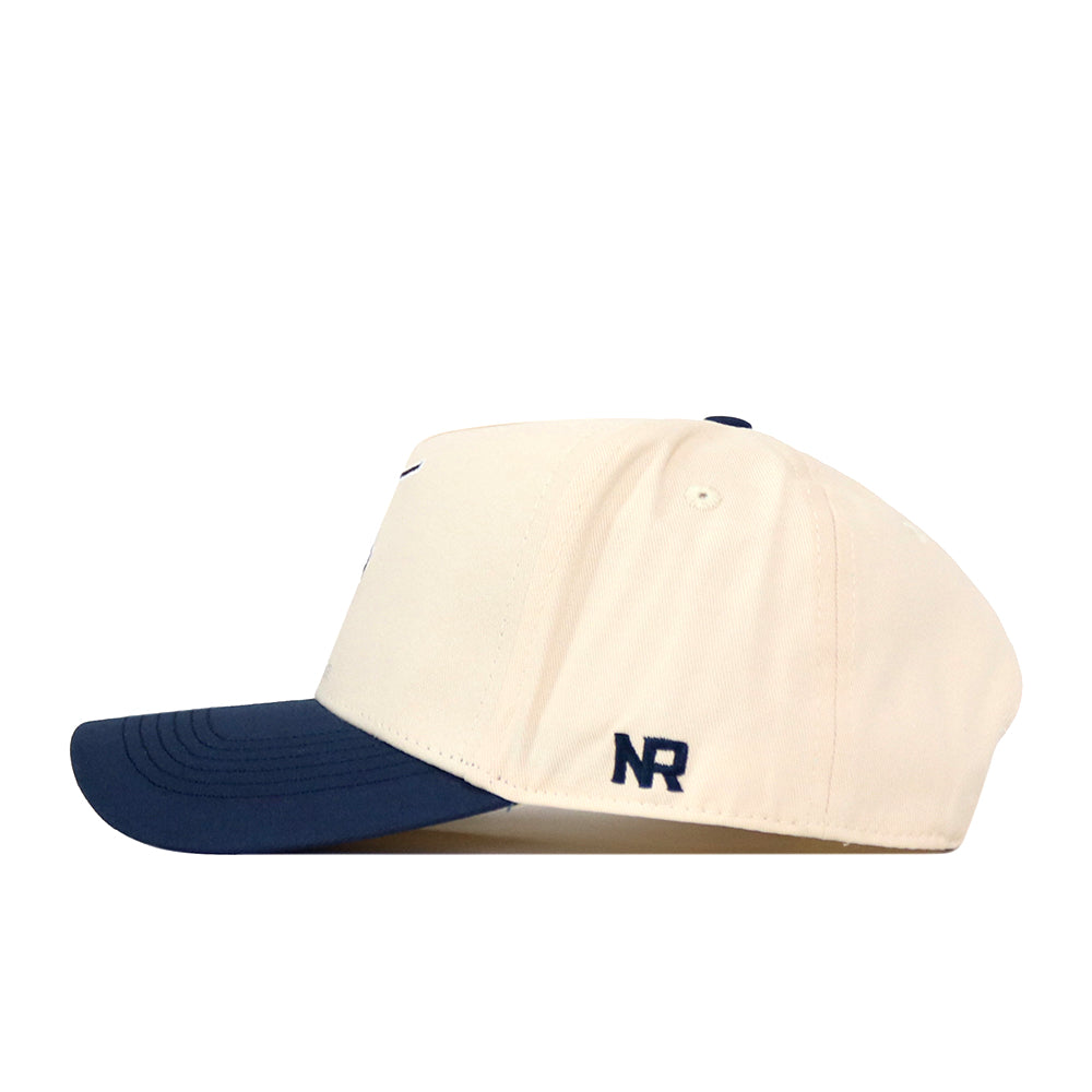 A cream-colored No Rivals WVU Mountaineers Mascot Patch Hat with a navy blue brim is shown in a side view. The letters NR are embroidered in navy on the side near the adjustable snap back, and the cap is crafted from high-quality performance fabric for comfort and durability.
