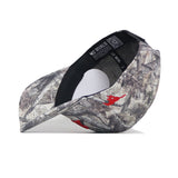 The SMU Outland Hat by No Rivals is a camouflage snapback with a curved bill, shown from the side. Made from high-quality cotton, it blends gray and brown hues with red accents. The inner lining reads "NO RIVALS.