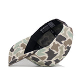 The Oklahoma Huntsman Hat by No Rivals is displayed angled from the bottom, showing its black sweatband and inner "NO RIVALS" label. This 5-panel duck camo cap rests on a white surface.