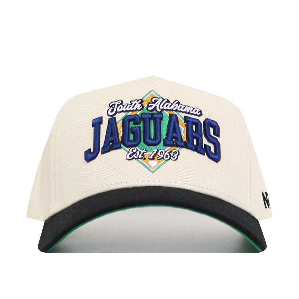 The No Rivals South Alabama Ballpark Hat is a cream-colored cotton cap with “South Alabama Jaguars Est. 1963” embroidered in blue, green, and gold. It features a black brim, green underside, structured fit, and an adjustable snapback closure.