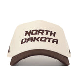 The North Dakota Espresso Hat by No Rivals features "NORTH DAKOTA" in striking brown lettering across the front, complemented by an embroidered logo for extra detail. This beige cap is finished with a coordinating brown brim and includes a snap back closure for easy size adjustment.