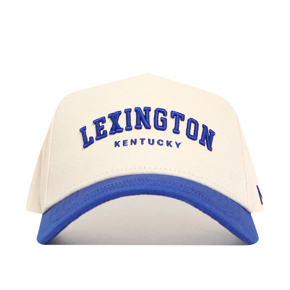 The Lexington Hometown Hat by No Rivals is a white cotton baseball cap with a blue brim, featuring "LEXINGTON KENTUCKY" embroidered in blue on the front and an adjustable snap back for a structured, comfortable fit.