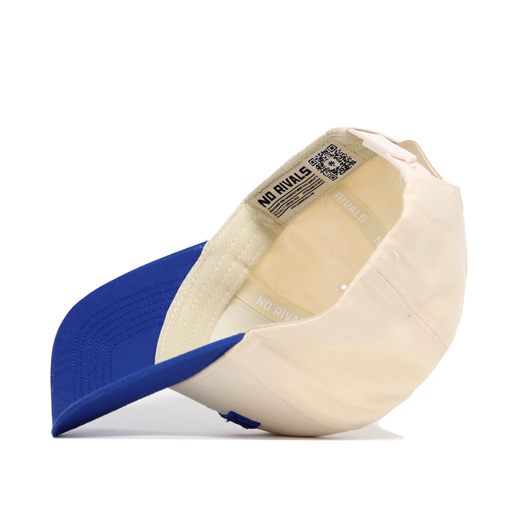 The Lexington Hometown Hat by No Rivals features a cream crown, blue brim, and adjustable snapback. Displayed upside down, its label shows the NO RIVALS branding and a QR code. Crafted from high quality cotton for superior comfort and fit.