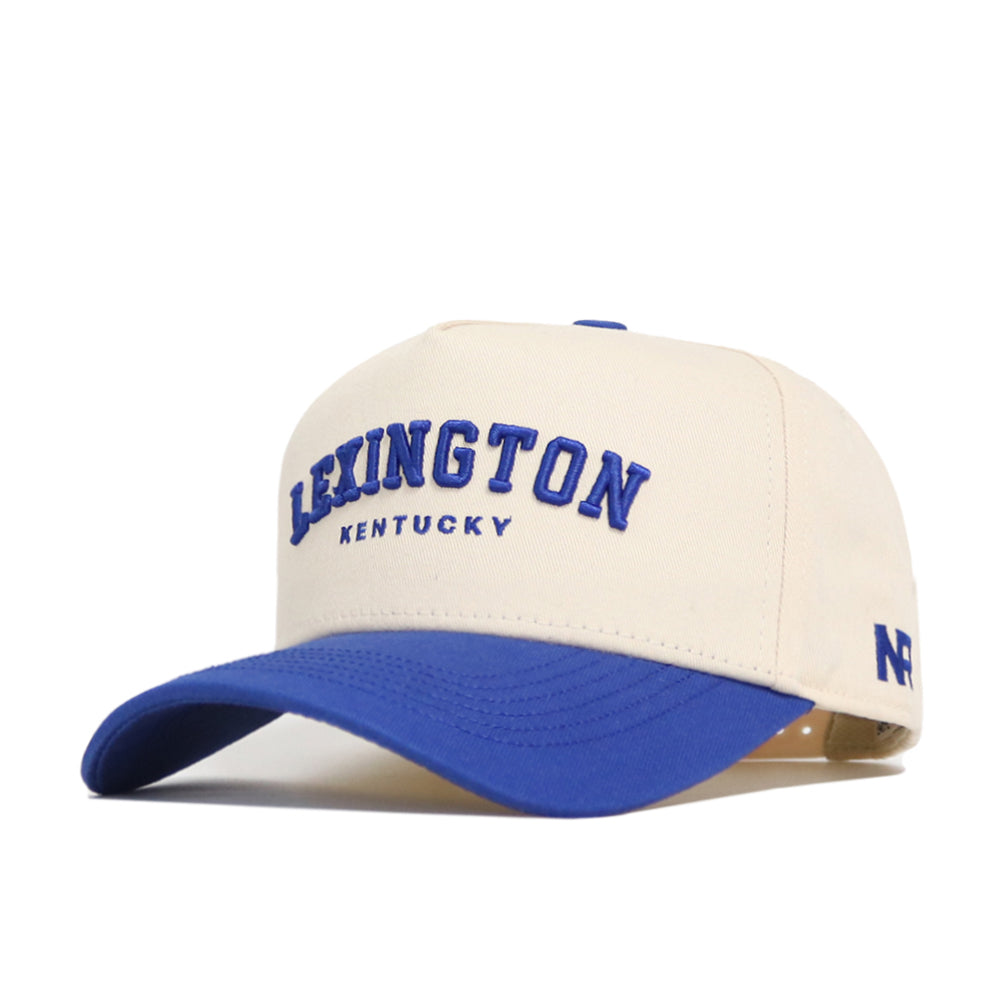 The Lexington Hometown Hat by No Rivals is a beige cotton baseball cap with "LEXINGTON KENTUCKY" embroidered in blue, a blue curved brim, NF logo on the side, and a structured fit for comfort.