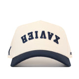 Show your support with the No Rivals Xavier Musketeers Upside Down Xavier Hat – Classic. This cream-colored snapback cap features a dark blue brim and the word XAVIER embroidered in navy blue letters upside down on the front, making it an officially licensed standout piece.