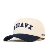 Show off your team pride with the officially licensed Xavier Musketeers | Upside Down Xavier Hat - Classic by No Rivals, a white and navy snapback featuring “XAVIER” in bold upside-down blue letters on the front and “NO RIV” embroidered on the side of the brim—a bold twist on classic spirit wear.