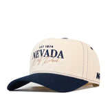 The No Rivals Nevada Wolf Pack Vintage Hat is a beige and navy blue baseball cap featuring “EST 1874 NEVADA Wolf Pack” embroidered on the front and “NV” on the side; this officially licensed cap includes a snap back closure for a comfortable, custom gameday fit.