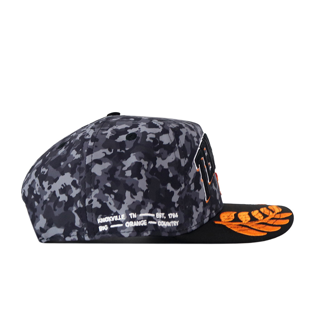 A side view of the No Rivals Tennessee Volunteers 2026 Military Appreciation Hat showcases its camo pattern and embroidered logo, featuring orange stitching on the black brim and white text on the side that reads “KNOXVILLE, TN EST. 1794 BIG ORANGE COUNTRY.” This officially licensed snapback cap delivers an authentic look and feel.