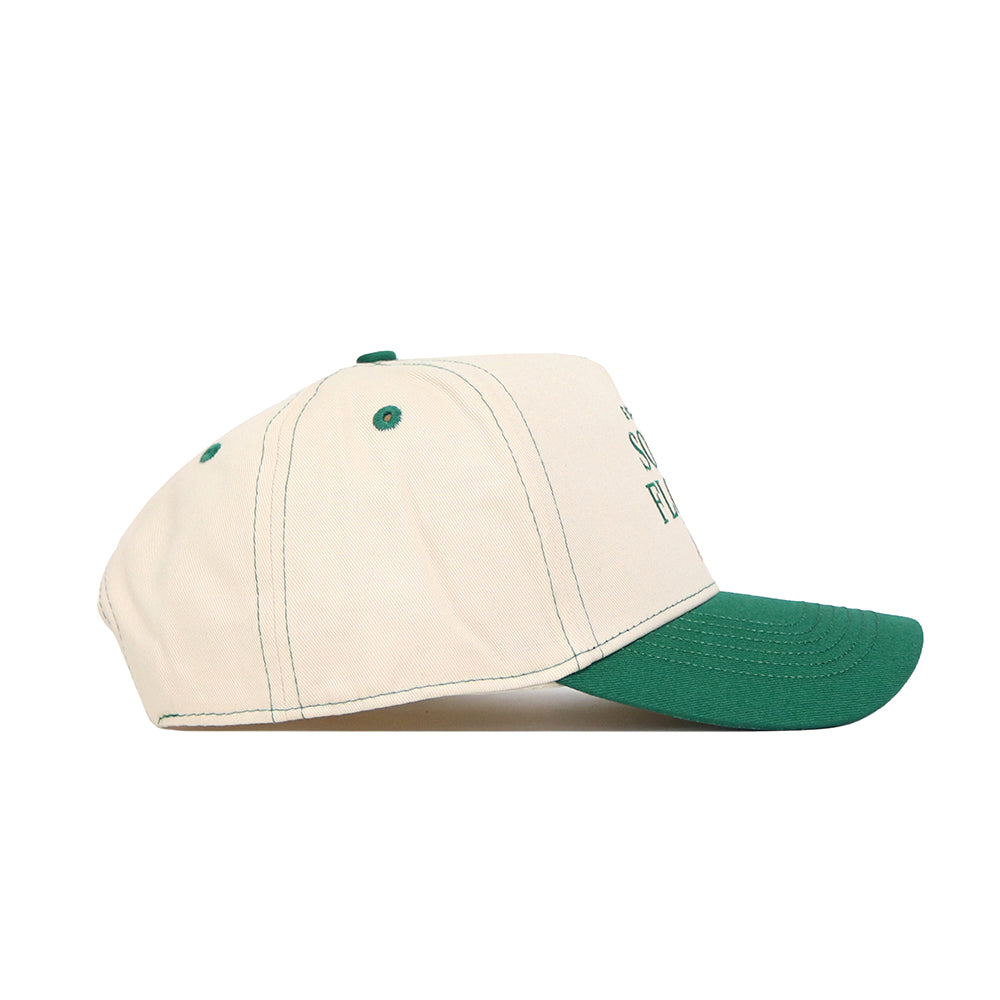 The No Rivals USF Vintage Hat is a cream snapback with a green brim, green stitching and eyelets, curved bill, and faint text on the front. Made of high-quality cotton and shown in a side view.
