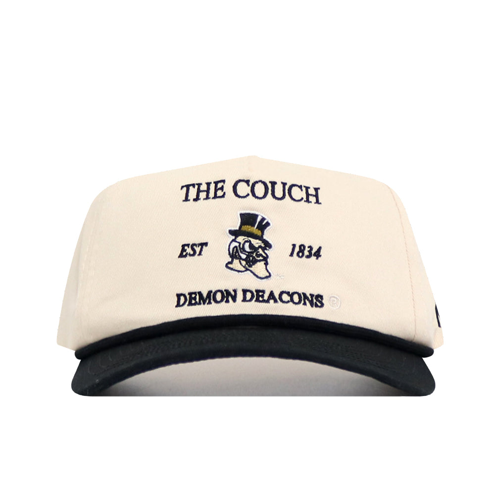 The No Rivals Wake Forest "The Couch" Walk-Off Hat is a cream cotton cap with a black brim, featuring an illustrated top-hat mascot and text: THE COUCH, EST 1834, DEMON DEACONS. Adjustable for comfort.