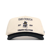 The No Rivals Wake Forest "The Couch" Walk-Off Hat is a cream cotton cap with a black brim, featuring an illustrated top-hat mascot and text: THE COUCH, EST 1834, DEMON DEACONS. Adjustable for comfort.